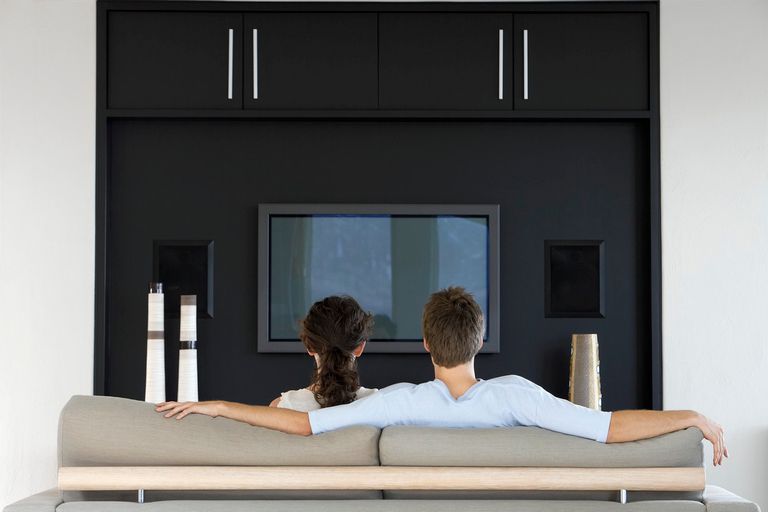 Two people sitting on a sofa looking at a TV with a home cinema system.