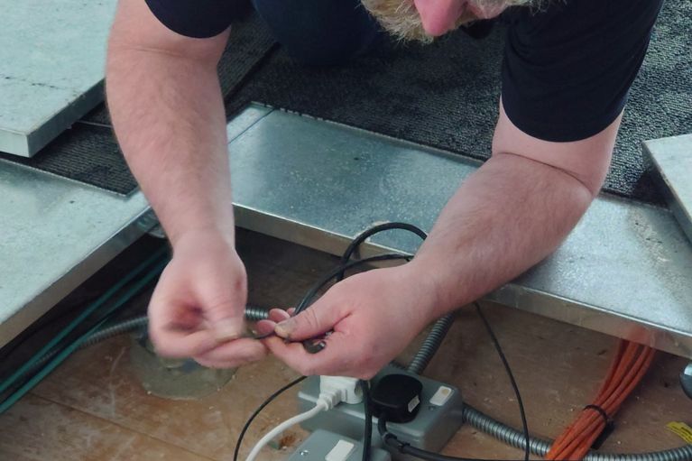 An engineer working on control wiring under a floor.